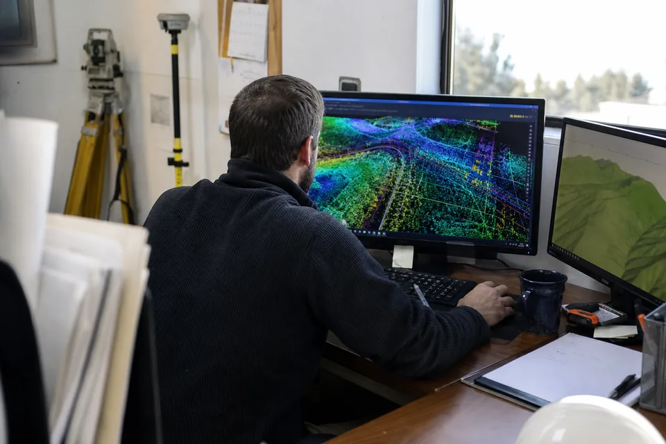 Survey CAD technician drawing breaklines over a drone point cloud on a desktop workstation